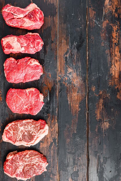 Conjunto de diferentes filetes de carne cruda con condimentos en la vista superior de tablones oscuros de madera vieja.