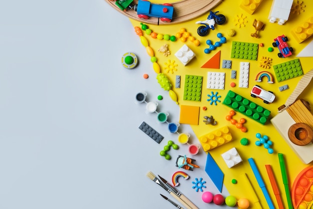 Conjunto de diferentes juguetes para niños, ferrocarril de madera, tren, constructor sobre una superficie amarilla y azul.