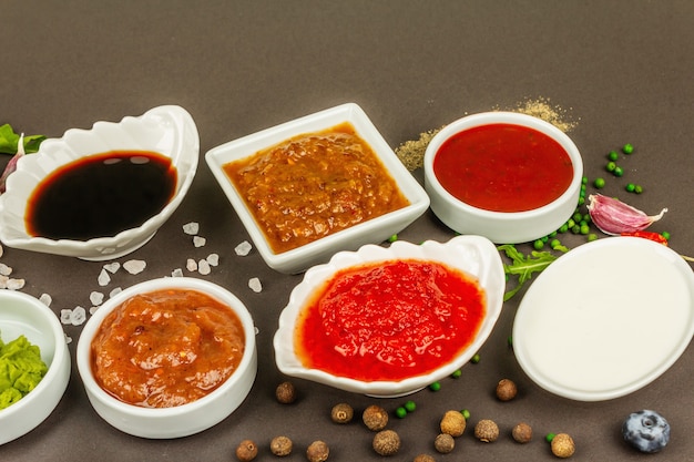 Conjunto de diferentes salsas: salsa de tomate, mayonesa, barbacoa, soja, salsa picante, wasabi, adjika, rábano picante, alioli, marinara. Fondo de hormigón de piedra oscura, cerrar