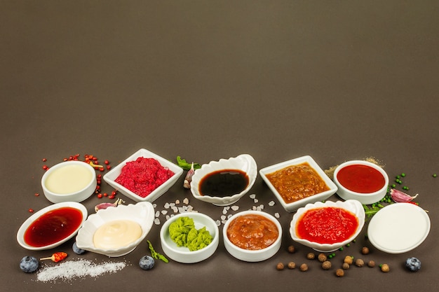 Conjunto de diferentes salsas: salsa de tomate, mayonesa, barbacoa, soja, salsa picante, wasabi, adjika, rábano picante, alioli, marinara. Fondo de hormigón de piedra oscura, espacio de copia