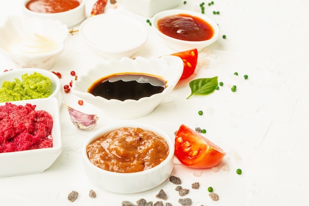 Conjunto de diferentes salsas: salsa de tomate, mayonesa, barbacoa, soja, salsa picante, wasabi, adjika, rábano picante, alioli, marinara. Luz dura de moda, sombra oscura. Fondo de masilla blanca, espacio de copia