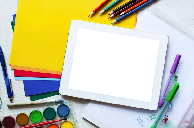 Conjunto escolar e material de escritório com tablet digital com lápis de tela branca em branco papel colorido tinta tesoura figuras e óculos em fundo branco de madeira conceito de educação