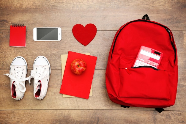 Conjunto escolar con mochila, teléfono móvil y zapatos sobre fondo de madera