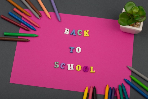 Conjunto escolar con texto en papel rosa Regreso a la escuela de letras de madera y crayones