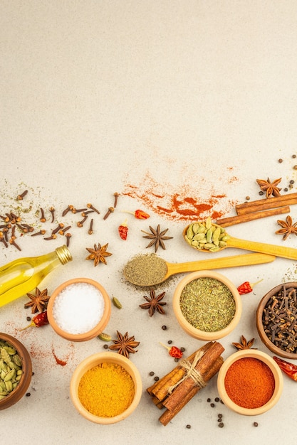 Un conjunto de especias para cocinar curry. Condimentos aromáticos: cúrcuma, pimentón, cardamomo, canela, anís estrellado, ají, pimienta negra, hierbas secas, sal. Fondo de hormigón de piedra clara, vista superior