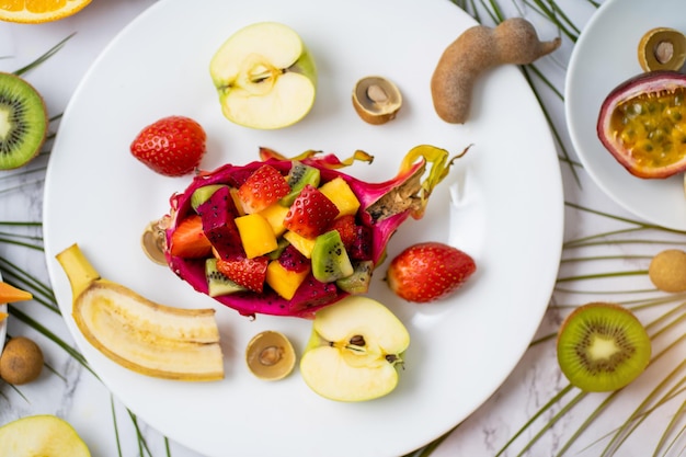 Foto conjunto de exóticas frutas tropicales de temporada jugosas maduras esparcidas en el plato y en la mesa. vista superior de frutas en rodajas y hojas tropicales. composición de verano laicos plana.