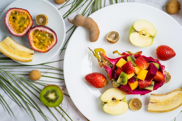 Conjunto de exóticas frutas tropicales de temporada jugosas maduras esparcidas en el plato y en la mesa. Vista superior de frutas en rodajas y hojas tropicales. Composición de verano laicos plana.