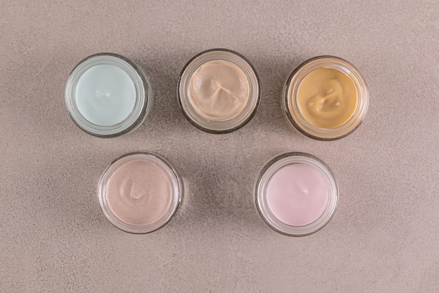 Un conjunto de frascos de vidrio con crema cosmética de diferentes colores para el cuidado de la piel de la cara y el cuerpo Diseño del embalaje Presentación del producto Maqueta de vista superior