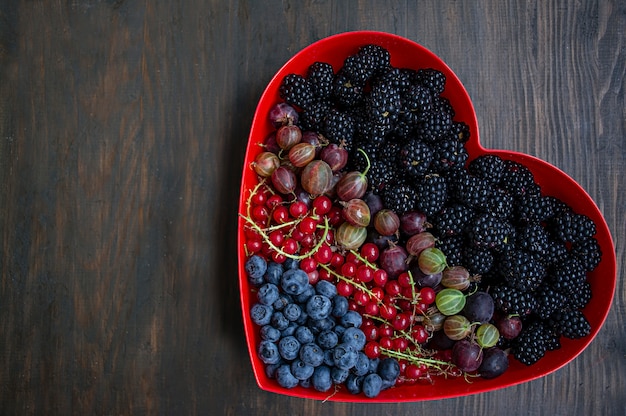 Conjunto de frutas frescas moras, grosellas, grosellas rojas, arándanos en una caja de corazón rojo