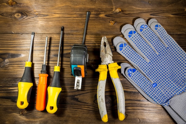 Conjunto de herramientas de trabajo sobre fondo de madera Destornilladores cinta métrica alicates y guantes