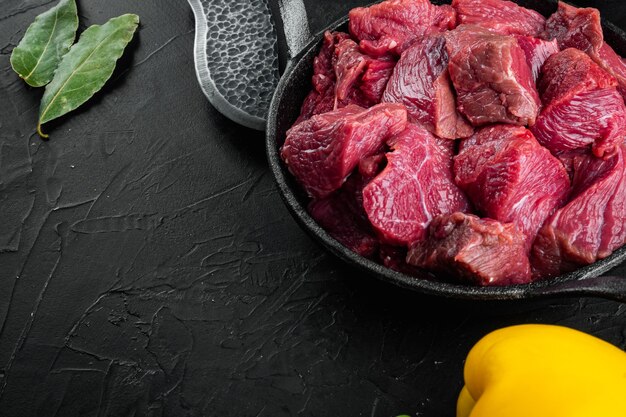 Conjunto de ingredientes de estofado de carne de res, en una sartén de hierro fundido, sobre una mesa de piedra negra