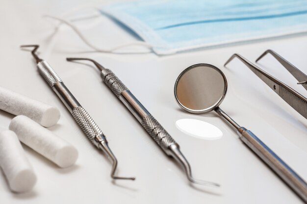 Conjunto de instrumentos dentales metálicos para tratamiento dental. Herramientas médicas y mascarilla protectora. Vista de primer plano. Poca profundidad de campo.