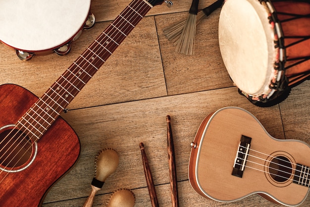 Conjunto de instrumentos musicales étnicos: pandereta, tambor de madera, pinceles, palos de madera, maracas y guitarras sobre suelo de madera. Concepto de música. Instrumentos musicales.