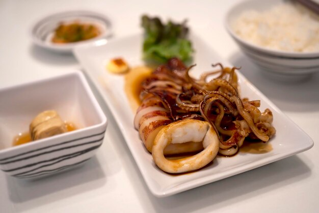 Un conjunto japonés de calamares a la parrilla con salsa de soja servido en un plato blanco con vegetales verdes