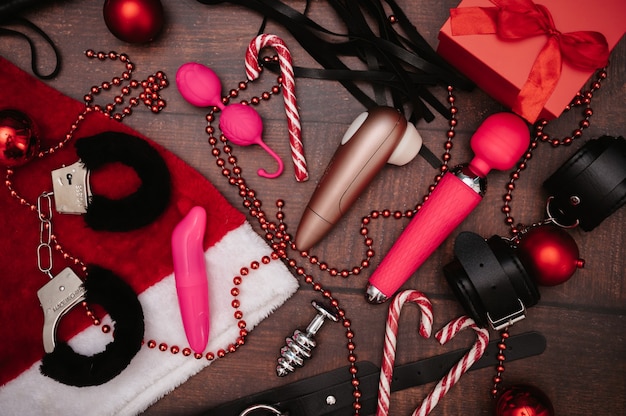 Un conjunto de juguetes BDSM para adultos con decoración navideña. Flatley. Esposas, látigo, masturbadores, plug anal, bolas navideñas.