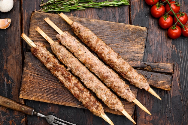 Conjunto de kebab de carne turca, en tablero de servicio, sobre fondo de mesa de madera oscura antigua, vista superior plana