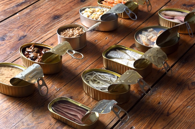 Conjunto de latas con pescado y marisco sobre fondo de madera, vista elevada y vista trasera