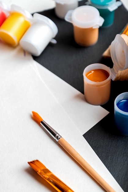 Conjunto de latas de pintura gouashe de color y pinceles para pintar sobre papel blanco listo para dibujar