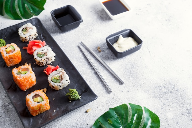 Conjunto de maki roll y hojas verdes de palma en la mesa de piedra.