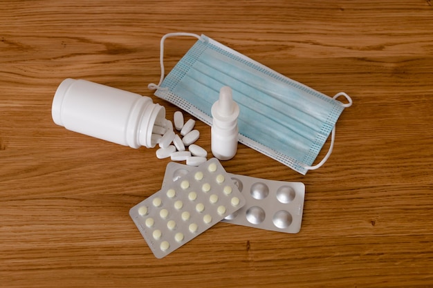 un conjunto de medicamentos en una mesa de madera. vitaminas, spray, pastillas en blisters, mascarilla médica.