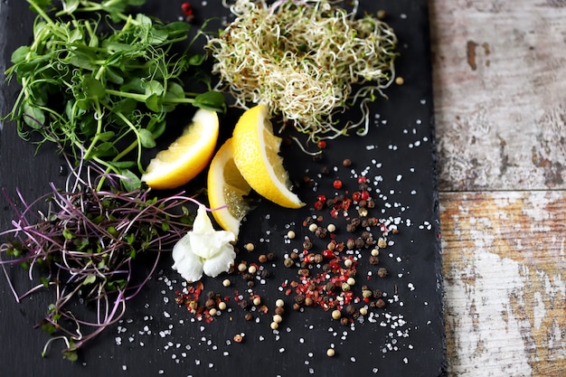 Conjunto de microgreens y especias en un tablero de piedra negro.