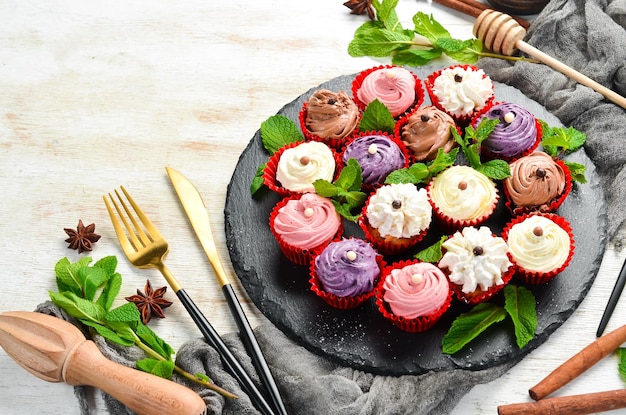 Conjunto de muffins de crema de colores en un plato negro con menta Vista superior Estilo rústico