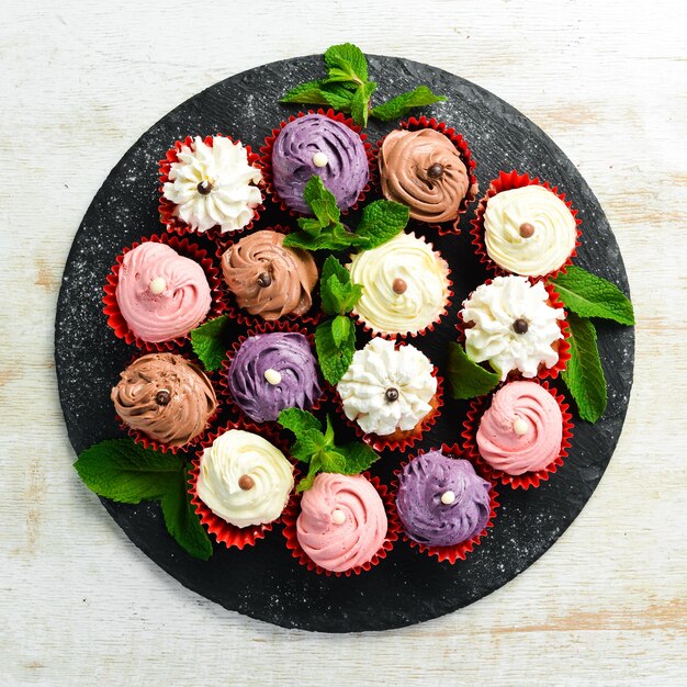 Conjunto de muffins de crema de colores en un plato negro con menta Vista superior Estilo rústico