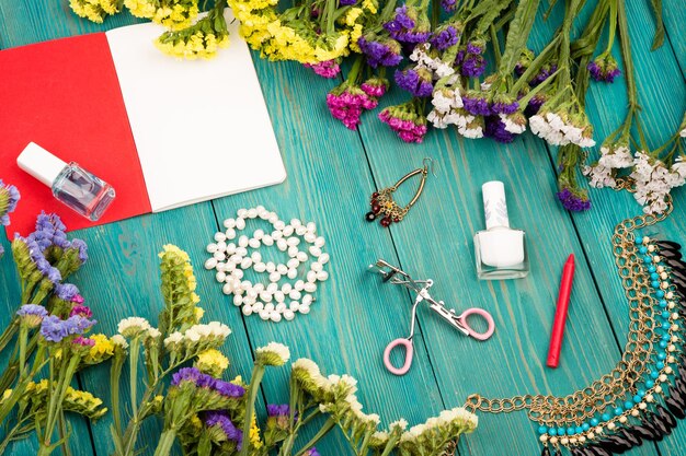 Foto conjunto de mujeres de verano con flores de colores cosméticos maquillaje bloc de notas bijou y elementos esenciales sobre fondo de madera azul