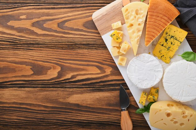 Conjunto o surtido de quesos Maasdam queso ahumado camembert queso azul parmesano queso brie con albahaca y pimienta sobre tablero de mármol blanco fondo antiguo de madera marrón Vista superior Espacio de copia libre