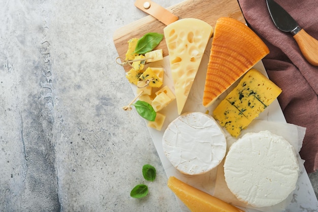 Conjunto ou variedade de queijos Maasdam queijo defumado camembert queijo azul parmesão queijo brie com manjericão e pimenta na placa de mármore branco fundo velho de madeira branca Vista superior Espaço para cópia grátis