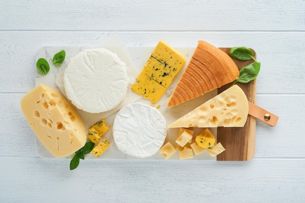 Conjunto ou variedade de queijos Maasdam queijo defumado camembert queijo azul parmesão queijo brie com manjericão e pimenta na placa de mármore branco fundo velho de madeira branca Vista superior Espaço para cópia grátis