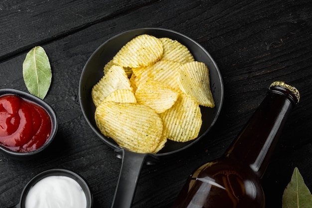 Conjunto de papas fritas y botella de cerveza, en la mesa de madera negra, vista superior plana