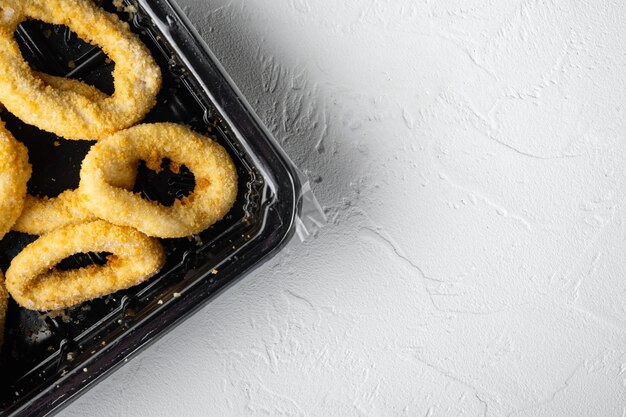 Foto conjunto de paquetes de anillos de calamares fritos, sobre fondo de mesa de piedra blanca, vista superior plana, con espacio para copiar texto