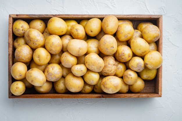 Conjunto de patatas baby frescas sin pelar, en caja de madera, sobre mesa de piedra blanca, vista superior plana