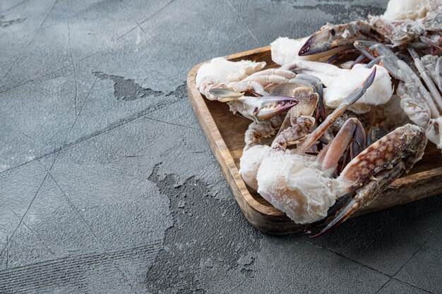 Conjunto de piezas de cangrejo de natación azul crudo congelado, en bandeja de madera, sobre mesa gris