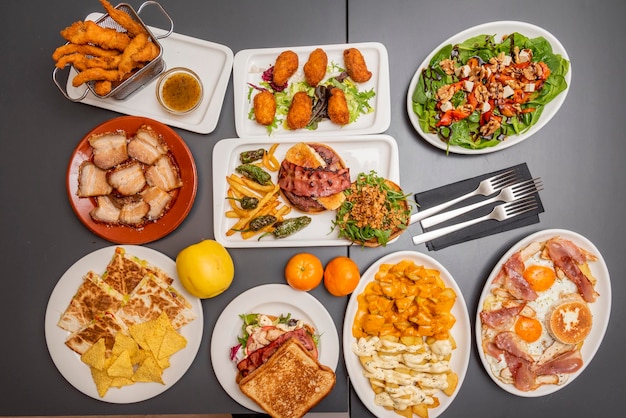 Conjunto de platos cocinados en un popular restaurante de tapas españolas Croquetas de jamón tocino frito huevos rotos patatas bravas hamburguesa con pimientos ensalada de espinacas