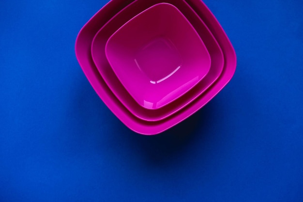 Conjunto de platos de color rosa sobre fondo azul. Utensilios de plástico para la cocina. Vista superior. Estilo minimalista. Copiar, espacio vacío para texto