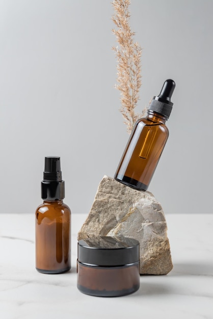 Conjunto de productos cosméticos para el cuidado de la piel. Concepto de presentación de envases sin marca. Suero facial, lituina, crema facial en frascos de vidrio ámbar con piedras naturales y junco seco de la pampa.