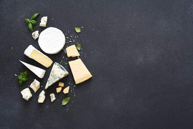 Conjunto de quesos: moho azul, parmesano, brie sobre fondo negro de hormigón.