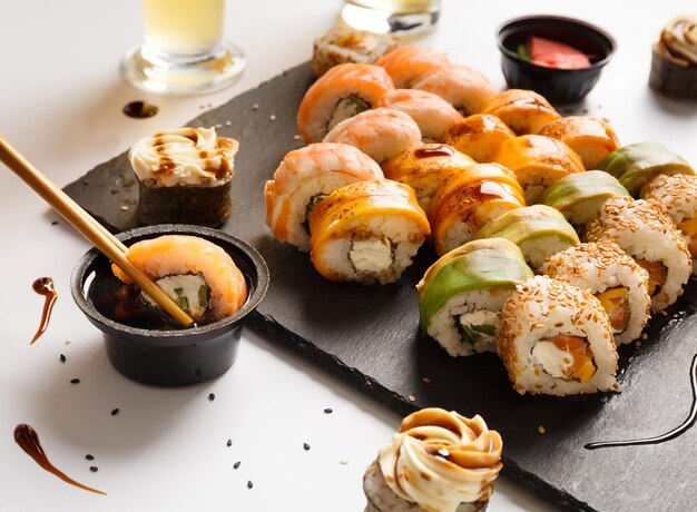 Foto conjunto de rollos de sushi con camarón, salmón, aguacate en un plato de piedra, un rollo sumergido en salsa de soja