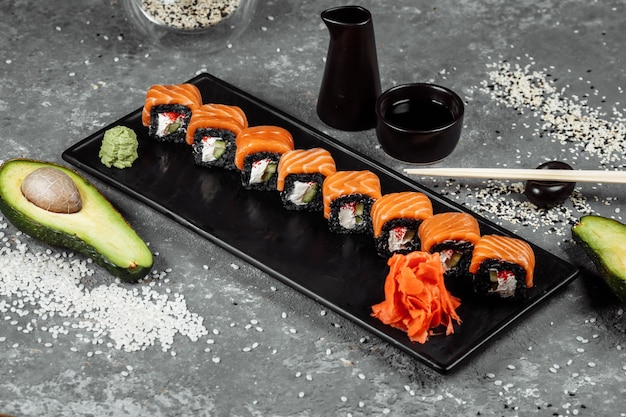 Un conjunto de rollos de sushi Filadelfia con pescado rojo, queso crema y subida negra se encuentra en un barco de placa