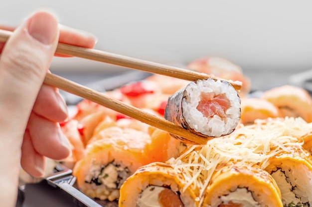Conjunto de rollos de sushi en un fondo blanco con palillos de bambú y una mano de mujer