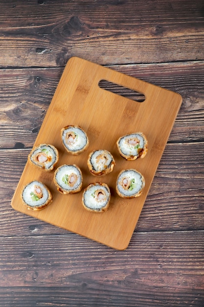 Conjunto de rollos de sushi frito caliente con salmón sobre tabla de madera.