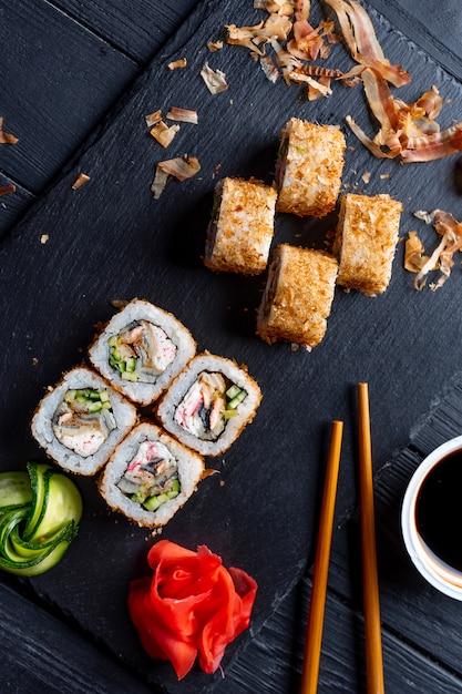 Conjunto de rollos de sushi con queso crema, arroz y cangrejo en un tablero negro decorado con jengibre y wassabi en una mesa de madera oscura. Cocina japonesa. Mesa de comida