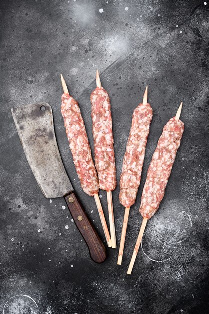 Conjunto de salchichas de kebabs de carne cruda kofta, sobre fondo de mesa de piedra oscura negra, vista superior plana