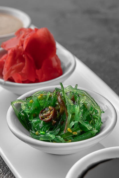 Conjunto de salsas para sushi en un plato blanco jengibre soja sésamo algas gris oscuro textura fondo vista lateral primer plano