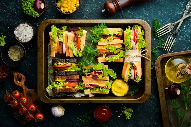 Un conjunto de sándwiches caseros con chorizo, chuleta, lechuga, cebolla, tomate y verduras. Estilo rústico. Espacio de copia libre.