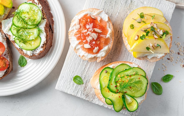 Un conjunto de sándwiches con verduras, frutas, mermelada, nueces y hierbas sobre un fondo claro Vista superior primer plano