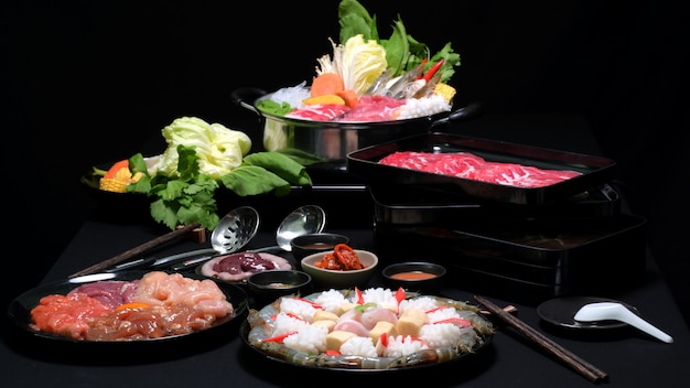 Conjunto de shabu shabu en olla caliente, carne fresca en rodajas, mariscos y verduras con fondo negro