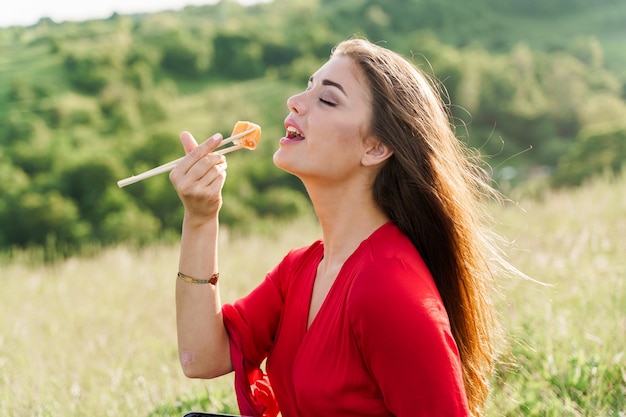 Foto conjunto de sushi y chica que se acerca a picar sushi en colinas verdes.